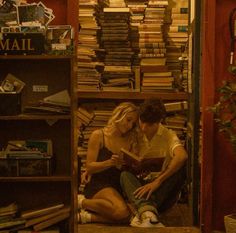 a man and woman sitting on the floor in front of a bookshelf full of books