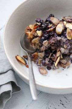 a bowl filled with cereal and nuts on top of a white table next to a spoon