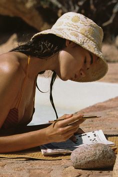 a woman in a hat is sitting on the ground and looking at her cell phone