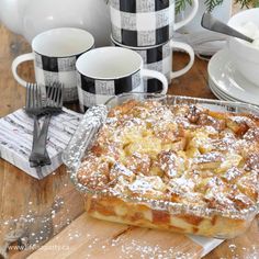 a pie sitting on top of a wooden table covered in powdered sugar next to cups and saucers