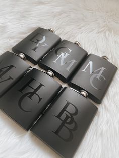 four black and white flasks with monogrammed letters are on a furry surface