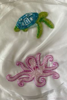 two different colored sea animals on a white sheet with pink and green thread work in the shape of an octopus