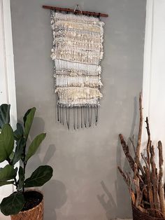 a wall hanging on the side of a gray wall next to potted plants