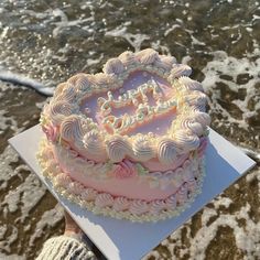 a pink heart shaped cake sitting on top of a white plate next to the ocean