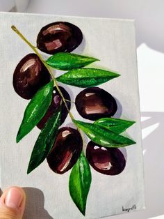 a painting of olives with green leaves on a white background is being held up by a hand