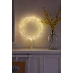 a white shelf with a vase filled with yellow flowers and a lighted wreath on top