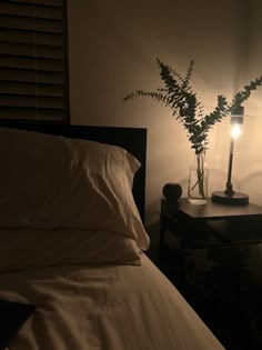 a bed with white sheets and pillows next to a night stand with a lamp on it