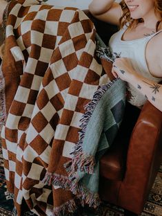 a woman sitting in a chair with a blanket on top of her and she is looking at the camera