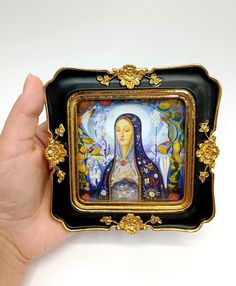 a hand holding a small tray with a painting on it's side and gold trimming around the edges