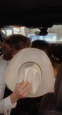 a man and woman sitting in the back seat of a car with hats on their heads