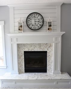 a white fireplace with a clock above it and candles on the mantle in front of it