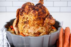 a roasted chicken in a roasting pan with carrots