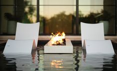 two white chairs sitting next to each other in front of a fire pit on top of a pool