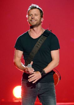 a male in a black shirt is holding a microphone and a red light behind him