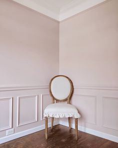 a white chair sitting in the corner of a room with pink walls and wooden floors