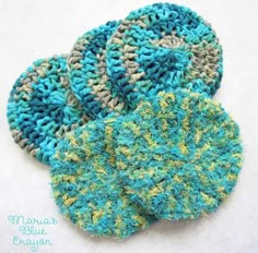 three crocheted coasters sitting on top of a white tablecloth covered in blue and green yarn