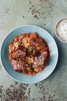 a blue plate topped with meat and rice next to a bowl filled with white rice