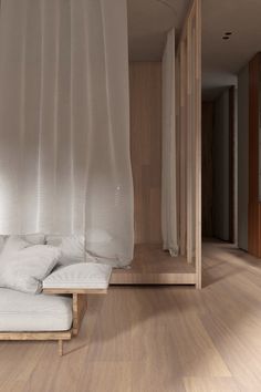 a bed sitting on top of a hard wood floor next to a white window curtain