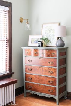 a chest of drawers in a room with a lamp and pictures on the top shelf