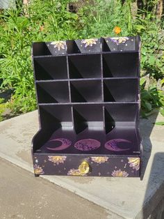 a purple and yellow flowered box with compartments on the outside, in front of some flowers