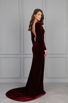 a woman in a long velvet dress standing against a wall with her back to the camera