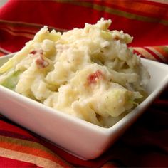 a white bowl filled with potato salad on top of a red and yellow table cloth