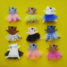 small stuffed animals in tutu skirts on a yellow surface with one cat wearing sunglasses