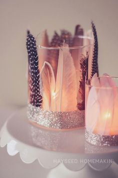 two candles are sitting on a table with feathers