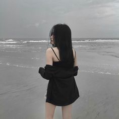 a woman standing on top of a beach next to the ocean with her back turned