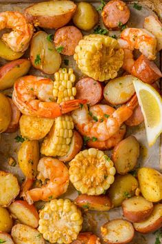 shrimp, corn and potatoes on a baking sheet with a lemon wedge in the middle