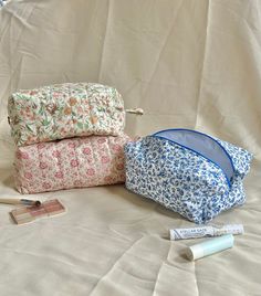 three cosmetic bags sitting on top of a bed next to some toothbrushes and an empty tube