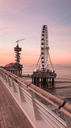 a ferris wheel sitting on top of a wooden pier next to the ocean at sunset