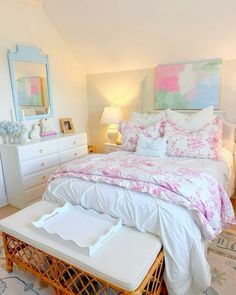 a white bed with pink and green comforter in a bedroom next to a dresser