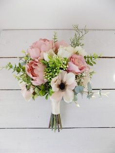 a bouquet of pink and white flowers sitting on top of a wooden table with greenery