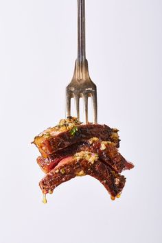 a fork with some food hanging from it's side and on top of another piece of meat