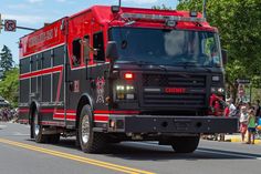 a red and black fire truck driving down the street with people standing in the background