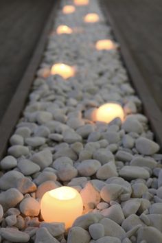 several lit candles sitting on top of rocks in the middle of a path that is lined with gravel