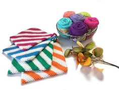 three crocheted dishcloths are next to a bowl of yarn and flowers