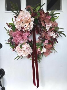 a wreath with pink and red flowers hanging on the front door, decorated with burgundy ribbon