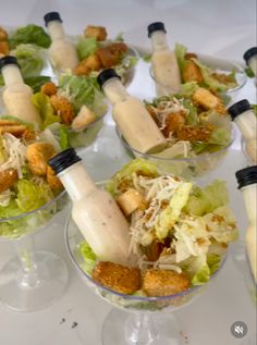 several glasses filled with salad and dressing sitting on a white tablecloth covered table top