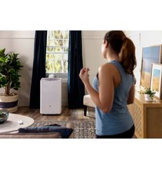 a woman standing in front of a window looking at an air purifier