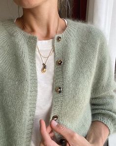 a woman is wearing a green cardigan and holding her hand out to the side