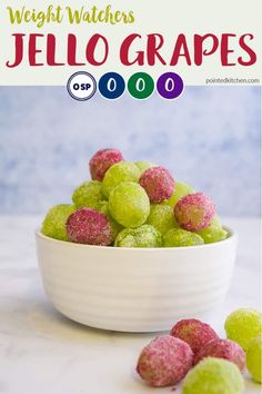 a white bowl filled with green and pink jello grapes on top of a counter