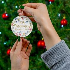 a person holding up a christmas ornament in front of a tree with ornaments