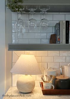 there is a shelf with wine glasses and books on it, along with a lamp