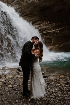 a bride and groom kissing in front of a waterfall