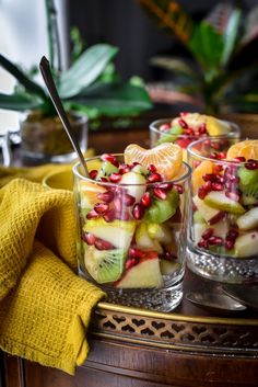 two glasses filled with fruit and pomegranate on top of a wooden table