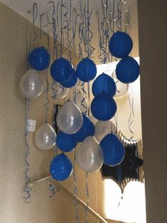 blue and white balloons are hanging from the ceiling in front of a mirror with streamers