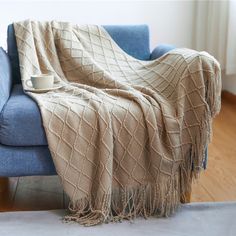 a blue chair with a blanket on it and a coffee cup sitting on the arm