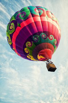 a large colorful hot air balloon flying through the blue sky with clouds in the background